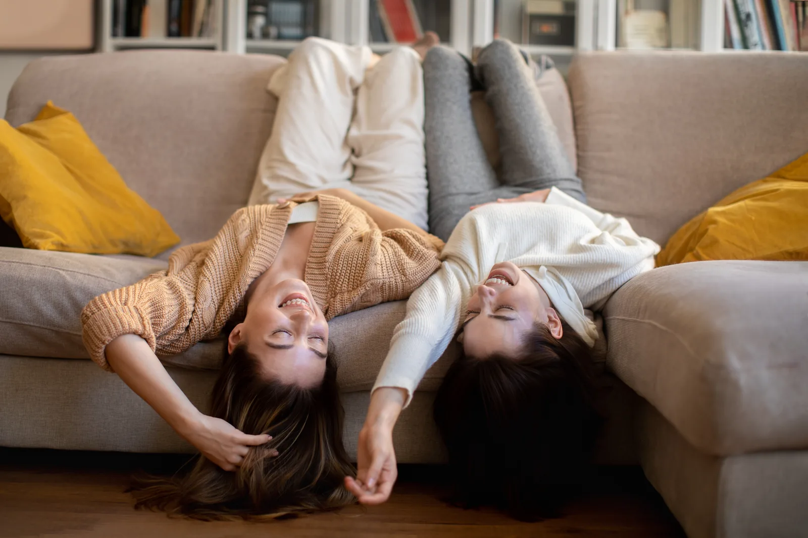 Zwei lachende Freundinnen liegen entspannt auf dem Sofa, menstruflow Ratgeber zum Mythos Periode synchronisieren